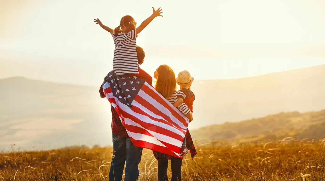 Family with an American flag walking together outdoors, a child on his father's shoulders